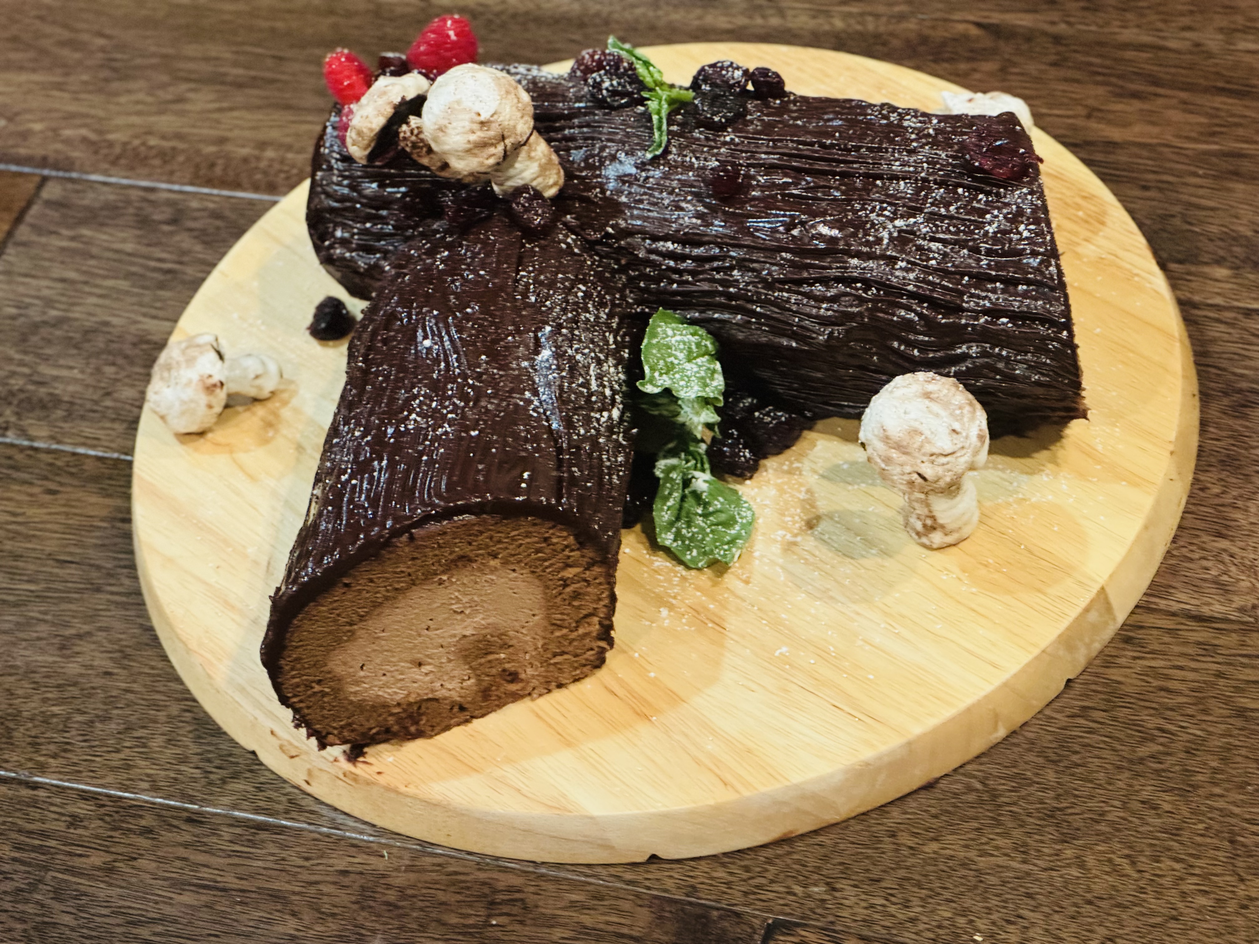 Artisanal chocolate Yule log cake decorated with berries and meringue mushrooms